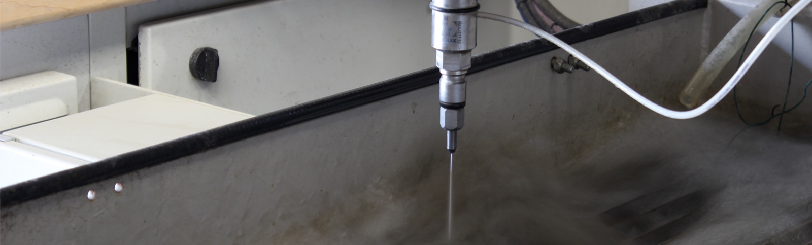 Waterstraal van de Omax-snijmachine die door metaal snijdt in het atelier van TAP