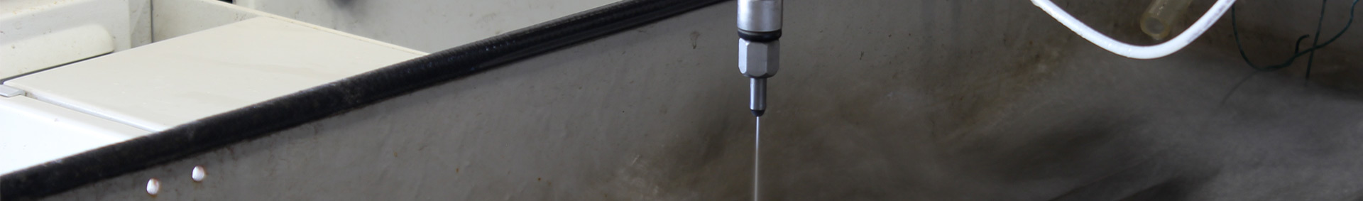 De waterstraalkop van de Omax-snijmachine van TAP boven het snijbed